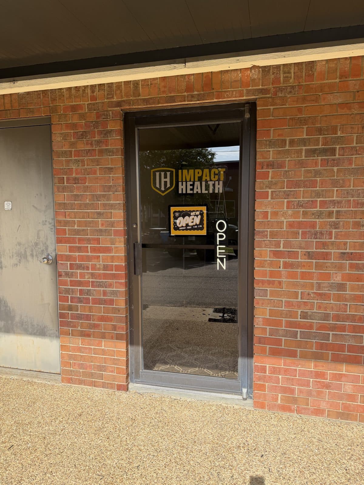 Impact Health Tupelo entrance on West Main Street with a We Are Open sign on the glass door