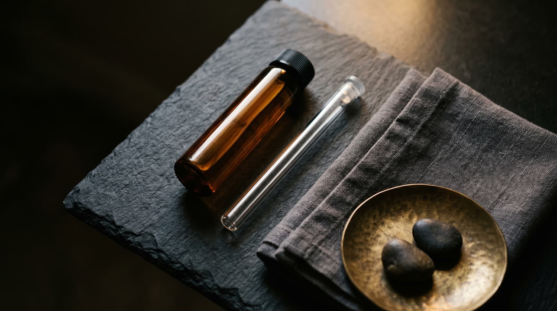 Amber testosterone vial and glass syringe on dark slate surface
